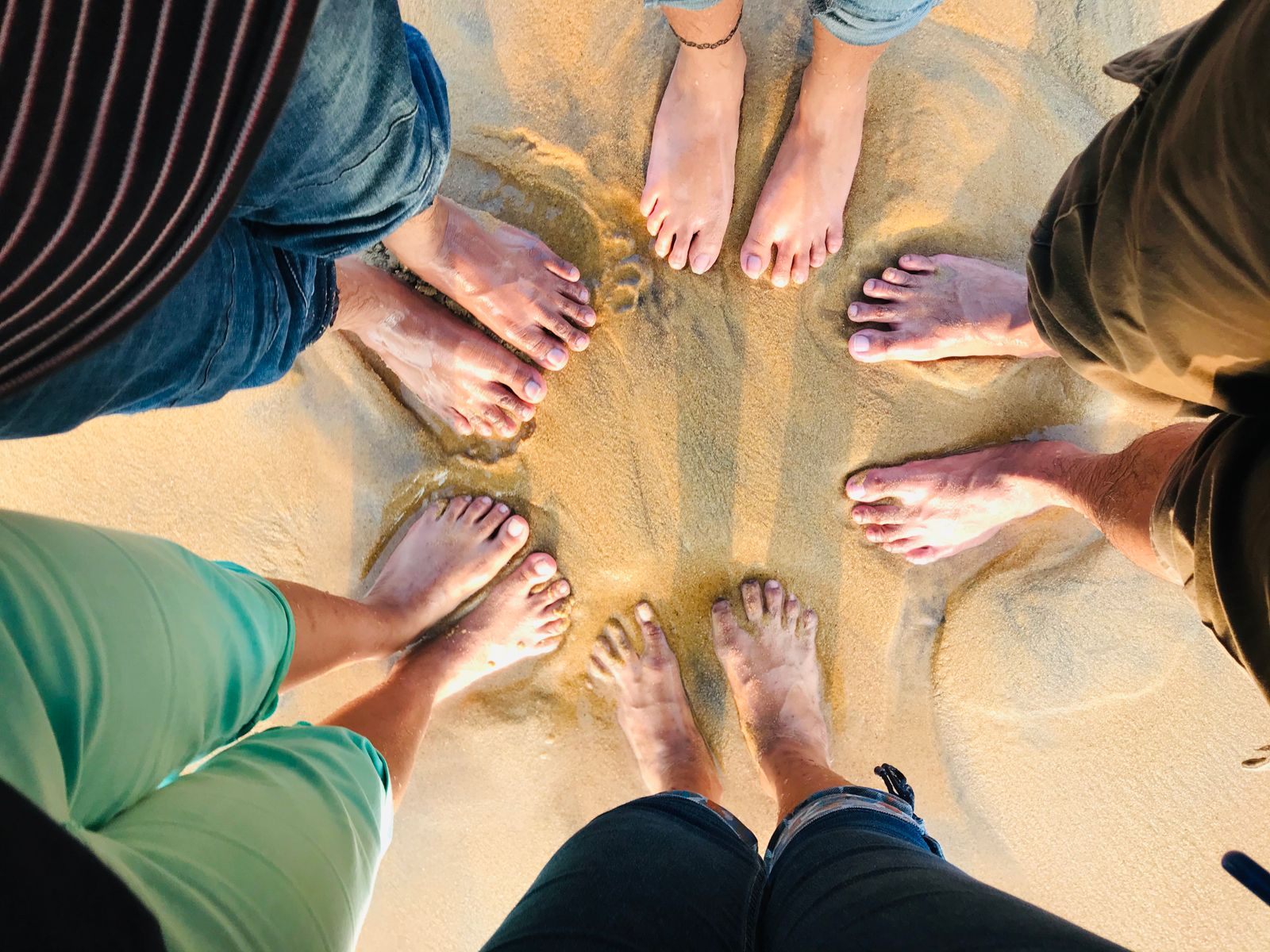 Bare feet of a group of friends forming a circle on sand