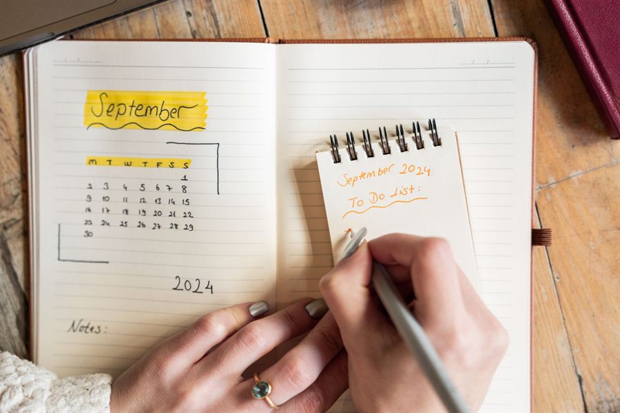 Hand writing in a planner beside a monthly calendar